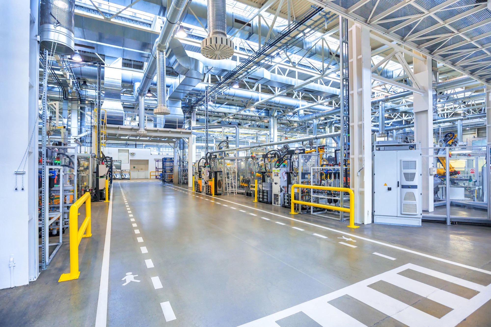 Interior of a modern manufacturing or industrial facility with machinery, ducts, and safety barriers.