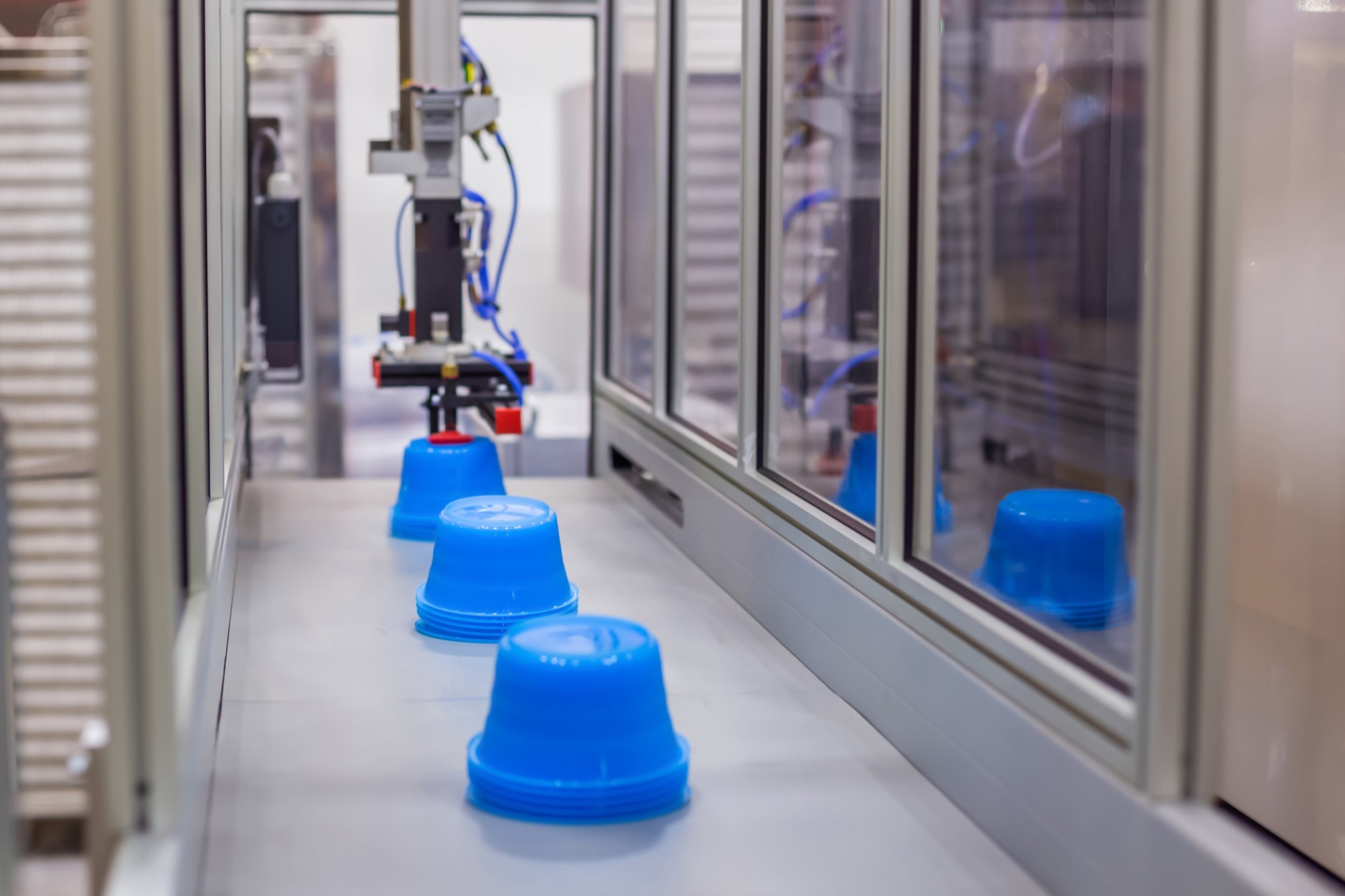 A robotics machine stacking blue plastic bowls inside a glass-enclosed manufacturing area.