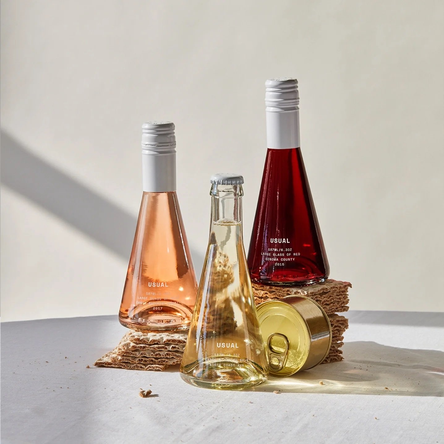 Three Usual single-serve wine bottles arranged with textured paper and natural lighting