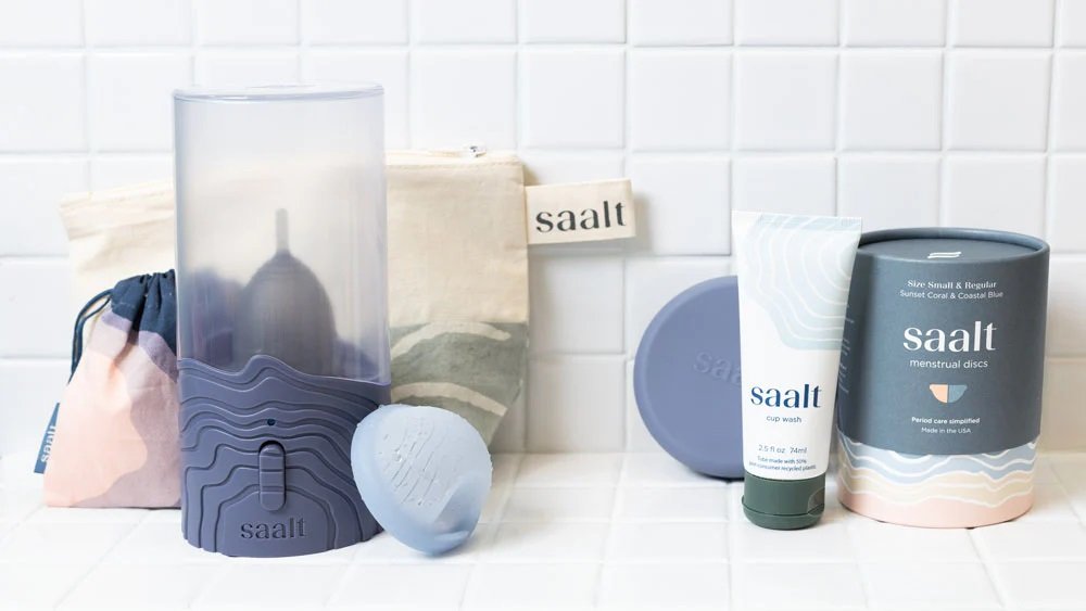 Saalt Steamer beside menstrual cup and storage pouch on bathroom counter