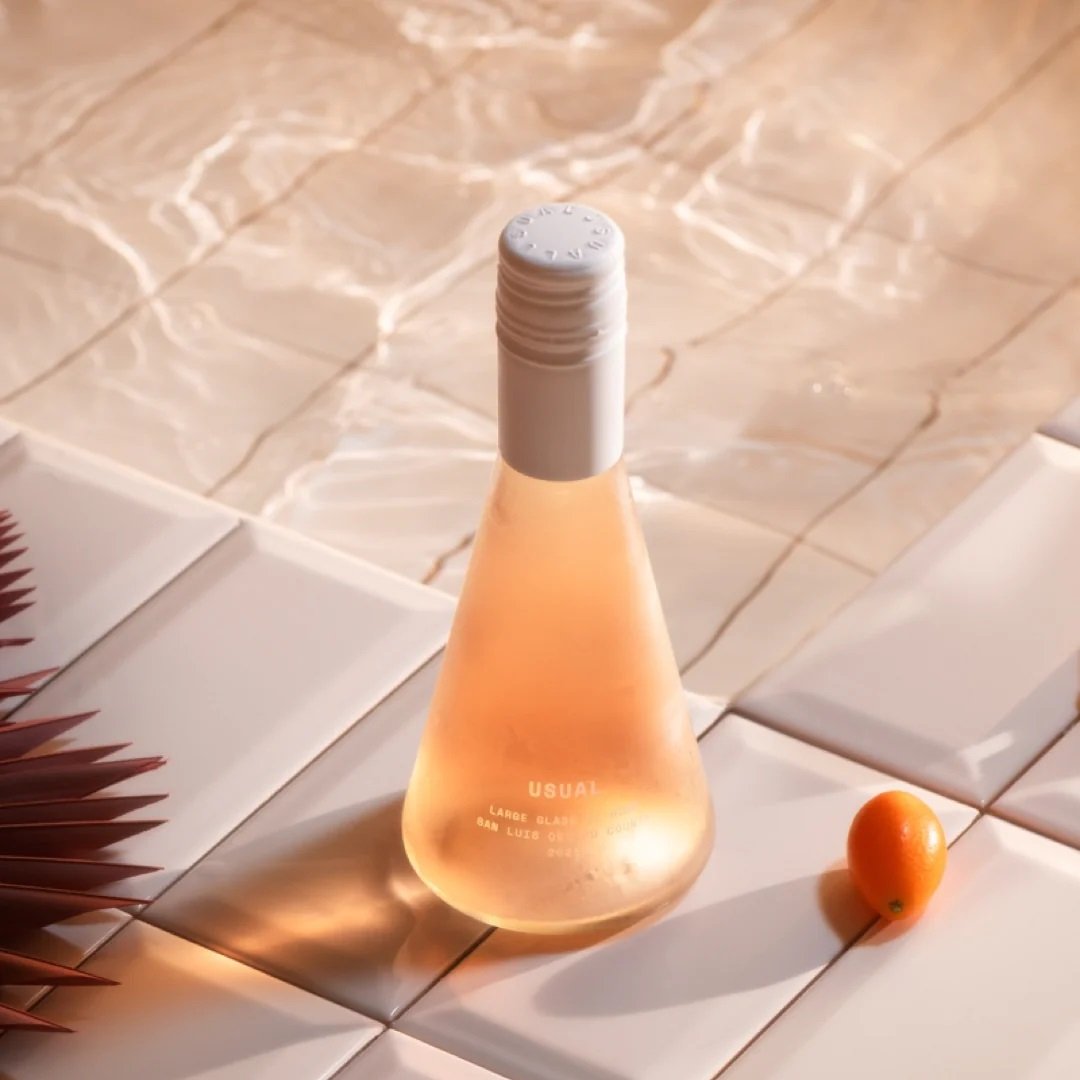 Usual wine bottle in warm lighting on a tiled white surface with a small orange object nearby